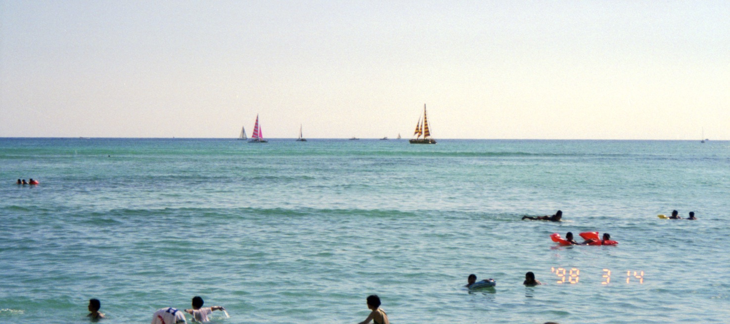 Photo looking out from shore at swimmers and sailboats.